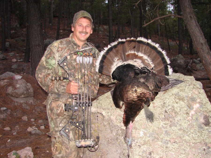 A man holding a bow and standing next to a turkey.