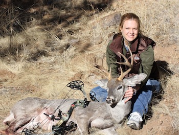 A woman sitting next to two deer with bow and arrow.